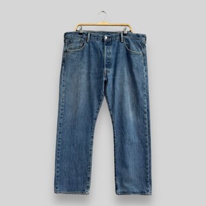 May include: A pair of blue denim jeans hanging on a wooden hanger. The jeans have a classic five-pocket style and a button fly.