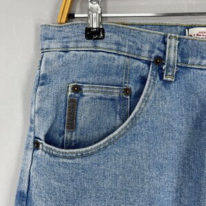 Puede incluir: Primer plano de unos vaqueros de mezclilla azul claro. Los vaqueros tienen un dise&ntilde;o cl&aacute;sico de cinco bolsillos con un bolsillo delantero visible. Las costuras son de un color contrastante y los vaqueros parecen desgastados.