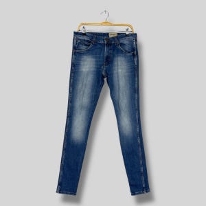 May include: Blue denim jeans hanging on a gold-colored hanger. The jeans have a classic five-pocket design, a button and zipper closure, and a faded wash. The jeans are straight-legged and appear to be new.