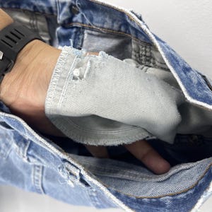 Pu&ograve; includere: Jeans in denim blu chiaro con un dettaglio usurato all'interno della gamba. Il denim &egrave; sfilacciato e strappato, rivelando il tessuto bianco sottostante.