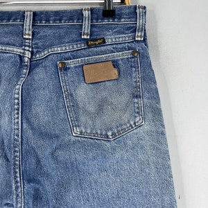 May include: A pair of blue denim jeans with a brown leather patch on the back pocket that says "Wrangler".