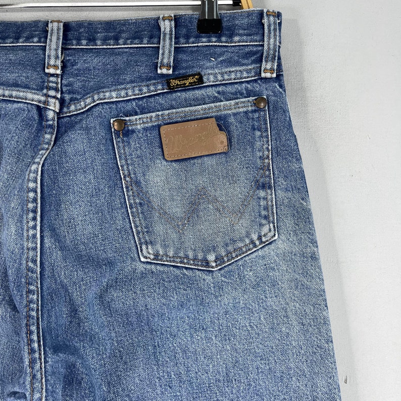 May include: A pair of blue denim jeans with a brown leather patch on the back pocket that says "Wrangler".