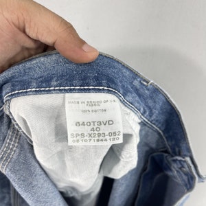 K&ouml;nnte beinhalten: Ein blaues Jeans-Etikett mit wei&szlig;en N&auml;hten, auf dem "MADE IN MEXICO OF U.S. FABRIC 100% COTTON 640T3VD 40 SPS-X293-052 051071944120" steht.