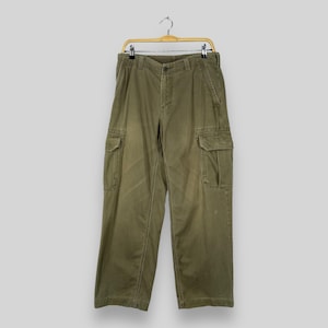 May include: A pair of olive green cargo trousers with multiple pockets. The trousers are hanging on a wooden hanger.