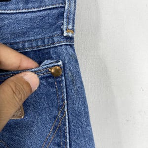 May include: Close-up of a blue denim pocket with a copper rivet. The pocket is part of a pair of jeans.