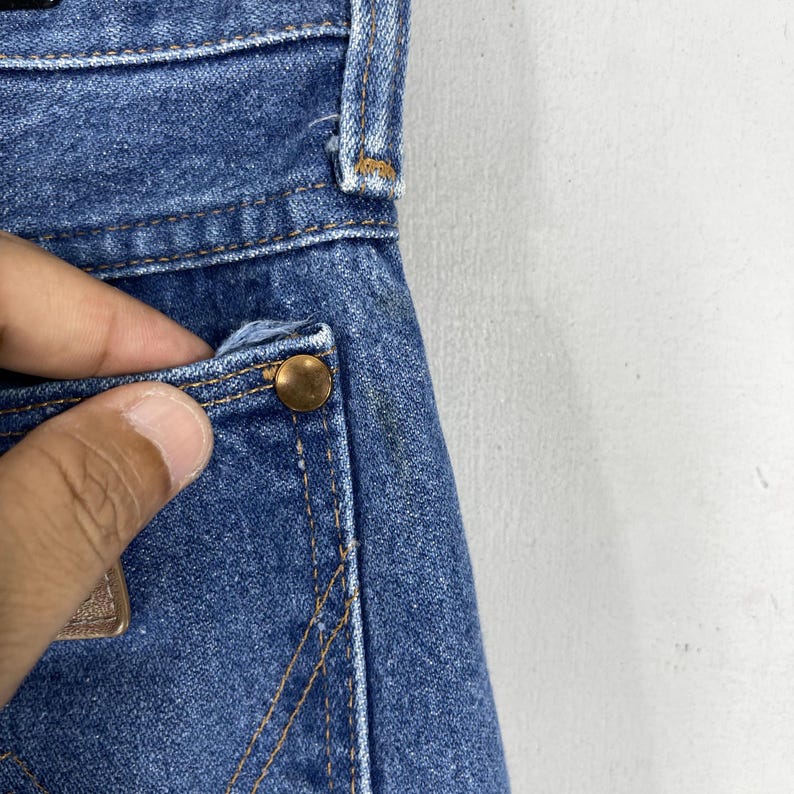 May include: Close-up of a blue denim pocket with a copper rivet. The pocket is part of a pair of jeans.