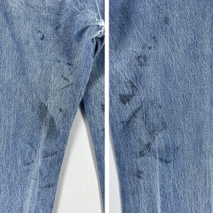 Pu&ograve; includere: Un paio di jeans blu denim con diverse macchie e segni scuri sul tessuto.