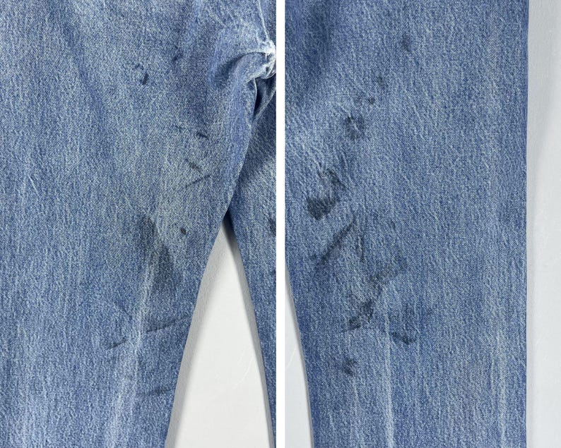 Pu&ograve; includere: Un paio di jeans blu denim con diverse macchie e segni scuri sul tessuto.