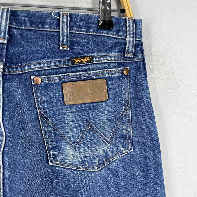 May include: A pair of blue denim jeans with a brown leather patch that says "Wrangler" on the back pocket.