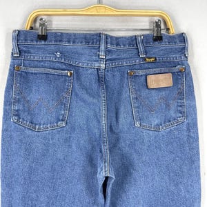 May include: A pair of blue denim jeans with a brown leather patch on the back pocket that says "Wrangler".