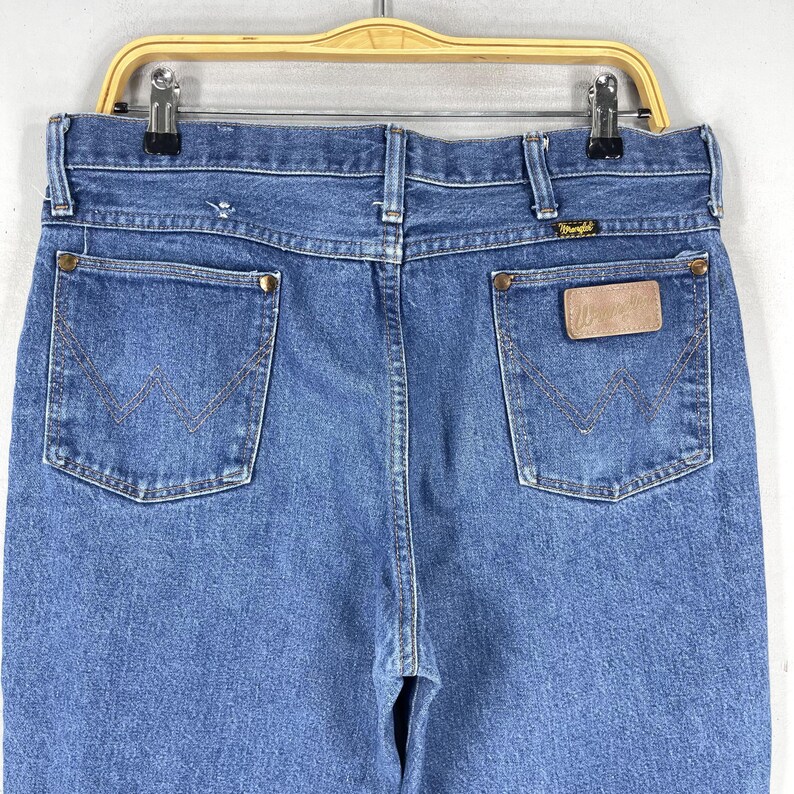 May include: A pair of blue denim jeans with a brown leather patch on the back pocket that says "Wrangler".