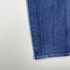 K&ouml;nnte beinhalten: Nahaufnahme des unteren Saums einer blauen Jeans. Der Saum ist mit hellbraunem Garn gen&auml;ht.