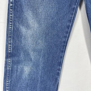 May include: Close-up of the denim fabric of a pair of blue jeans. The fabric has a faded, worn look.