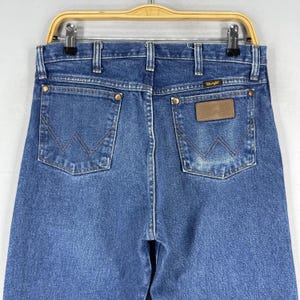 May include: A pair of blue denim jeans with a brown leather patch on the back pocket that says "Wrangler".