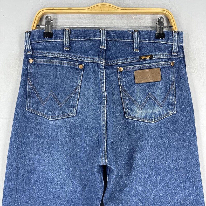 May include: A pair of blue denim jeans with a brown leather patch on the back pocket that says "Wrangler".