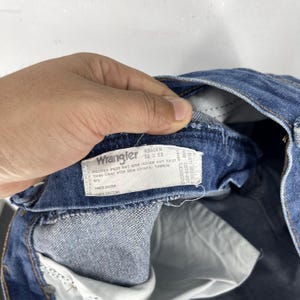 May include: A close-up of the inside of a pair of blue denim jeans with a white Wrangler tag that reads "936DEN 36 x 33" and "Machine wash hot and inside out first three times with like colours, tumble dry."