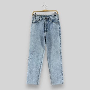 Pode incluir: Jeans de denim azul claro lavado com &aacute;cido com corte reto. As cal&ccedil;as est&atilde;o penduradas em um cabide de madeira.