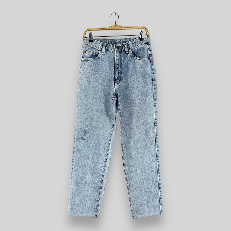 Pode incluir: Jeans de denim azul claro lavado com &aacute;cido com corte reto. As cal&ccedil;as est&atilde;o penduradas em um cabide de madeira.