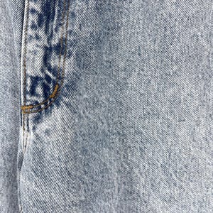 Pode incluir: Close-up de tecido de ganga azul claro com uma costura a correr verticalmente no lado esquerdo.