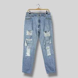 May include: Light blue denim jeans with distressed rips and tears. The jeans are hanging on a gold-colored hanger. The jeans have a classic five-pocket design and a button and zipper closure.