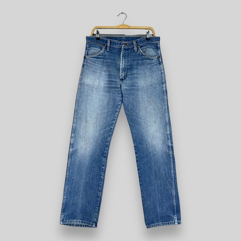 May include: A pair of blue denim jeans hanging on a gold hanger. The jeans have a classic straight leg style and are made of a soft, comfortable fabric.
