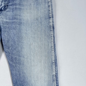 May include: Close-up of the side seam of a pair of light blue denim jeans. The seam is stitched with white thread.