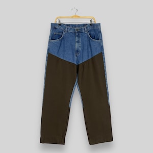K&ouml;nnte beinhalten: Eine Hose aus blauem Denim und braunem Canvas mit kontrastierendem Farbblock-Design. Die Hose hat eine gerade Beinweite und einen Knopfverschluss.