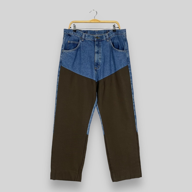 K&ouml;nnte beinhalten: Eine Hose aus blauem Denim und braunem Canvas mit kontrastierendem Farbblock-Design. Die Hose hat eine gerade Beinweite und einen Knopfverschluss.