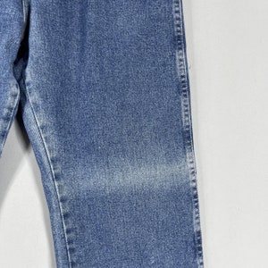 May include: Close-up of the denim fabric of a pair of blue jeans. The fabric has a faded look and a subtle texture.
