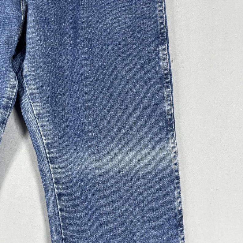 May include: Close-up of the denim fabric of a pair of blue jeans. The fabric has a faded look and a subtle texture.