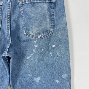 以下が含まれることがあります： 色あせた外観と白いペンキの飛沫がある、明るい青色のデニムジーンズ。ジーンズはバックポケットとクラシックな5ポケットデザインが特徴です。デニムは使い古された外観をしています。