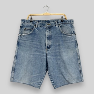 May include: A pair of light blue denim shorts with a button fly and belt loops. The shorts have a faded look and are hanging on a wooden hanger.