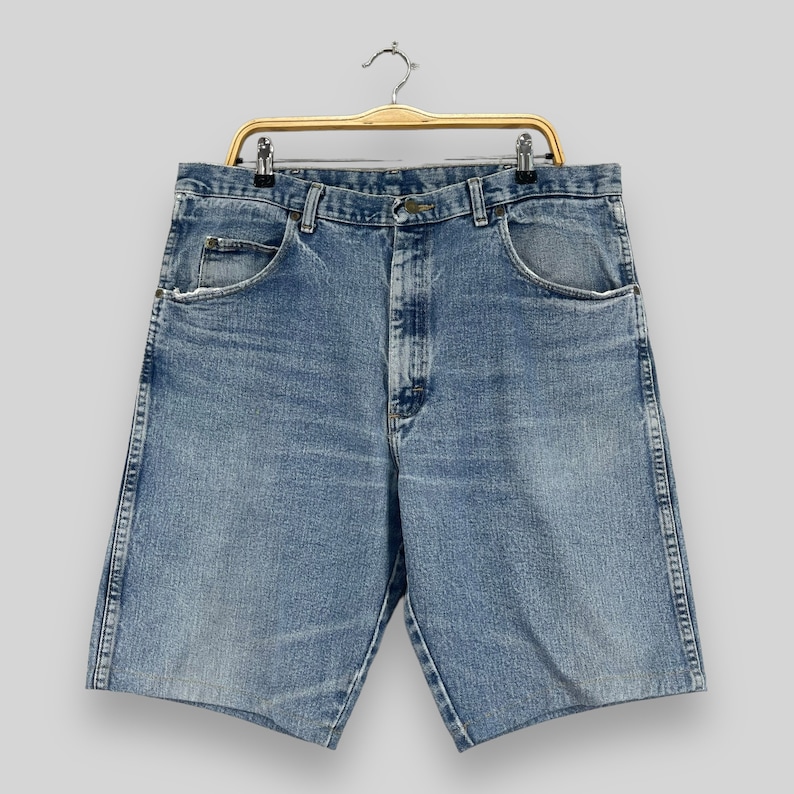 May include: A pair of light blue denim shorts with a button fly and belt loops. The shorts have a faded look and are hanging on a wooden hanger.