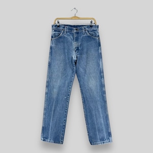 Pu&ograve; includere: Un paio di jeans blu denim appesi a un appendiabiti in legno. I jeans hanno uno stile classico a gamba dritta e sono realizzati in un tessuto morbido e confortevole.