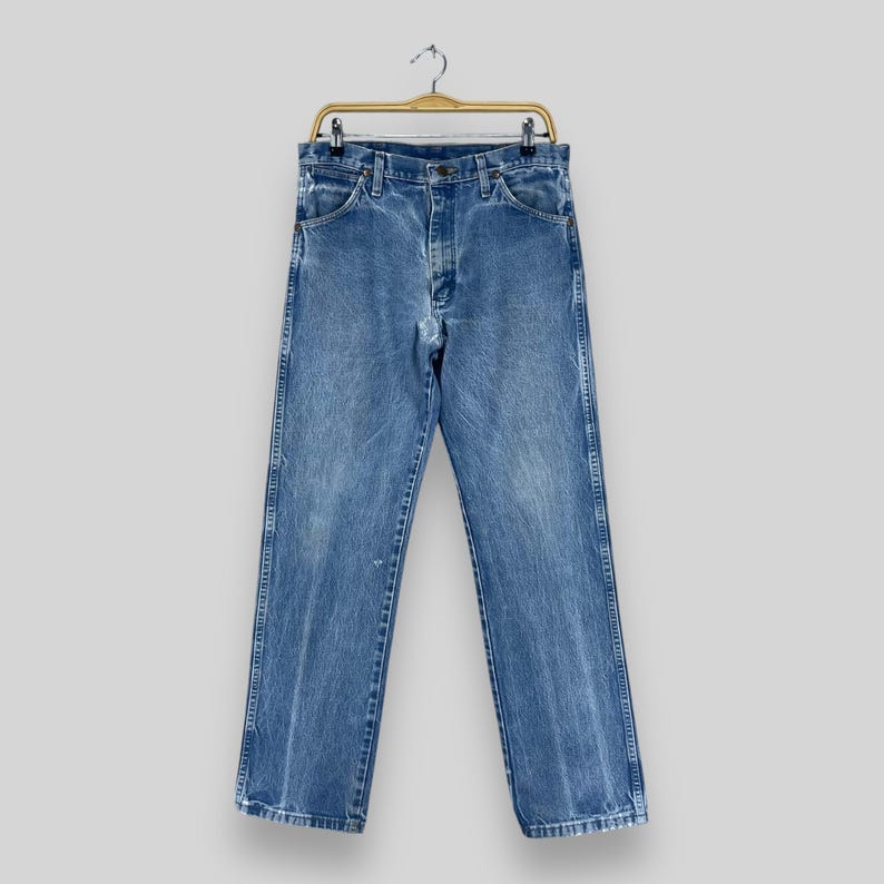 Pu&ograve; includere: Un paio di jeans blu denim appesi a un appendiabiti in legno. I jeans hanno uno stile classico a gamba dritta e sono realizzati in un tessuto morbido e confortevole.
