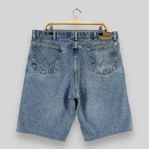 May include: A pair of blue denim shorts with a brown leather Wrangler label on the back right pocket. The shorts have a classic five-pocket design and a relaxed fit.