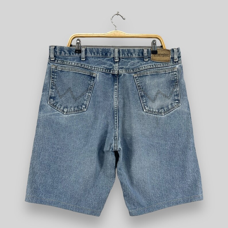 May include: A pair of blue denim shorts with a brown leather Wrangler label on the back right pocket. The shorts have a classic five-pocket design and a relaxed fit.