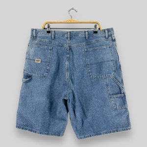 K&ouml;nnte beinhalten: Eine blaue Jeans-Arbeitshose mit mehreren Taschen und einem Markenetikett auf der linken Tasche.