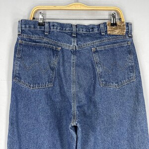 K&ouml;nnte beinhalten: Eine blaue Jeanshose mit einem braunen Leder-Patch am hinteren Bund. Der Patch tr&auml;gt den Schriftzug "Wrangler".