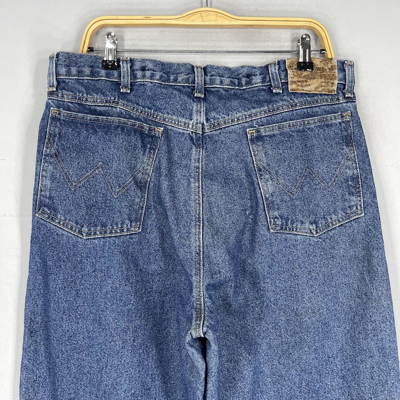 K&ouml;nnte beinhalten: Eine blaue Jeanshose mit einem braunen Leder-Patch am hinteren Bund. Der Patch tr&auml;gt den Schriftzug "Wrangler".