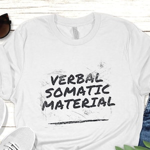 Könnte beinhalten: Weißes T-Shirt mit dem Text "VERBAL SOMATIC MATERIAL" in schwarzer Schrift mit einem Used-Look.