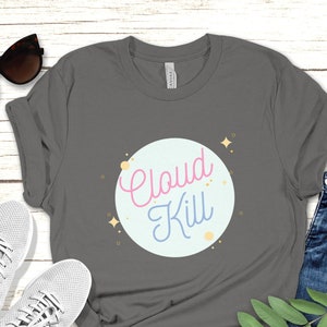 以下が含まれることがあります： グレーのTシャツに、薄い青色の円の中にピンクと青の文字で「Cloud Kill」と書かれています。円は小さな金色の星で囲まれています。