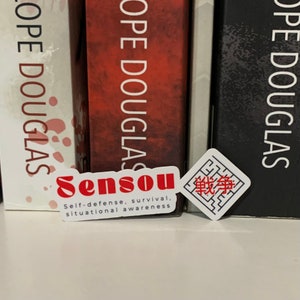 May include: Two stickers are positioned in front of a row of books. One sticker features the word "Sensou" in red, with the text "Self-defence, survival, situational awareness" below. The other sticker has Japanese characters.