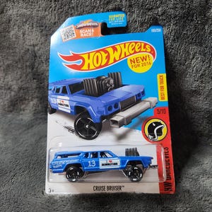 May include: A blue Hot Wheels Cruise Bruiser toy car on a blue and red card. The car has black wheels and the number 13 on the side. The card reads "NEW! FOR 2016" and "BEST FOR TRACK".