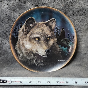 May include: A decorative plate featuring a detailed portrait of a wolf with yellow eyes against a starry night sky. The plate has a gold rim and the artist's name, Peter Kull, is visible.