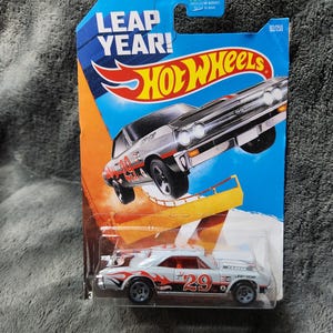 May include: A Hot Wheels die-cast toy car in its original packaging. The car is white with red and orange flames and the number 29. The packaging is blue and orange with the words "LEAP YEAR!" and "Hot Wheels".
