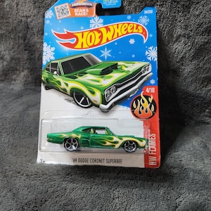 May include: A Hot Wheels die-cast toy car of a green '69 Dodge Coronet Superbee with flame graphics. The car is in a blue and white package with the Hot Wheels logo and the text "HW Flames". The package also includes the text "Scan & Race!"