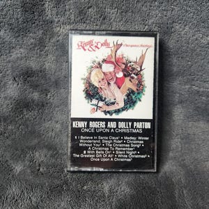 May include: A vintage cassette tape featuring Kenny Rogers and Dolly Parton's "Once Upon a Christmas" album. The cover art depicts the duo with Santa Claus and a reindeer in a festive wreath. Track titles are listed below the album title.