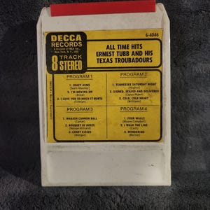 May include: An 8-track stereo tape of "All Time Hits" by Ernest Tubb and His Texas Troubadours. The label is yellow with black text and a red top. The track list includes songs like "Crazy Arms" and "I Walk the Line."