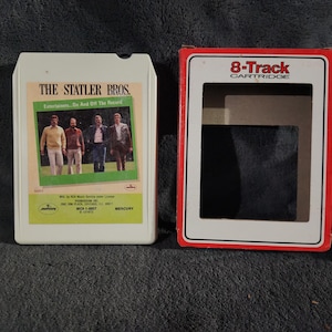 May include: An 8-track cartridge and its case. The cartridge is white with a green and yellow label featuring a photo of The Statler Bros. The case is red and white, labeled "8-Track CARTRIDGE".